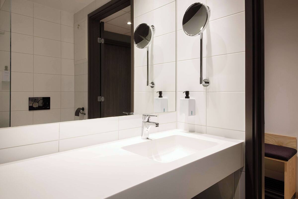 A modern bathroom with a white sink, two round mirrors, and a wooden bench.