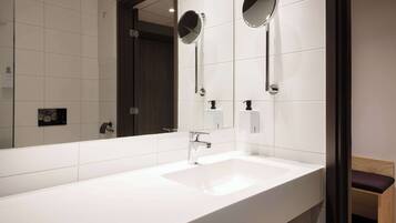 Un baño moderno con un lavabo blanco, dos espejos redondos y un banco de madera.