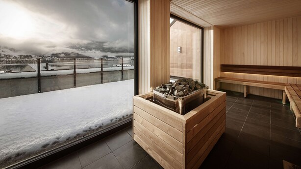 A modern interior with a wooden bench, a stone fireplace, and a large window overlooking a snowy landscape. - Scandic Voss (Voss)