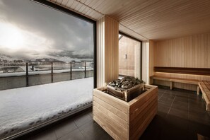A modern interior with a wooden bench, a stone fireplace, and a large window overlooking a snowy landscape. - Scandic Voss (Voss)