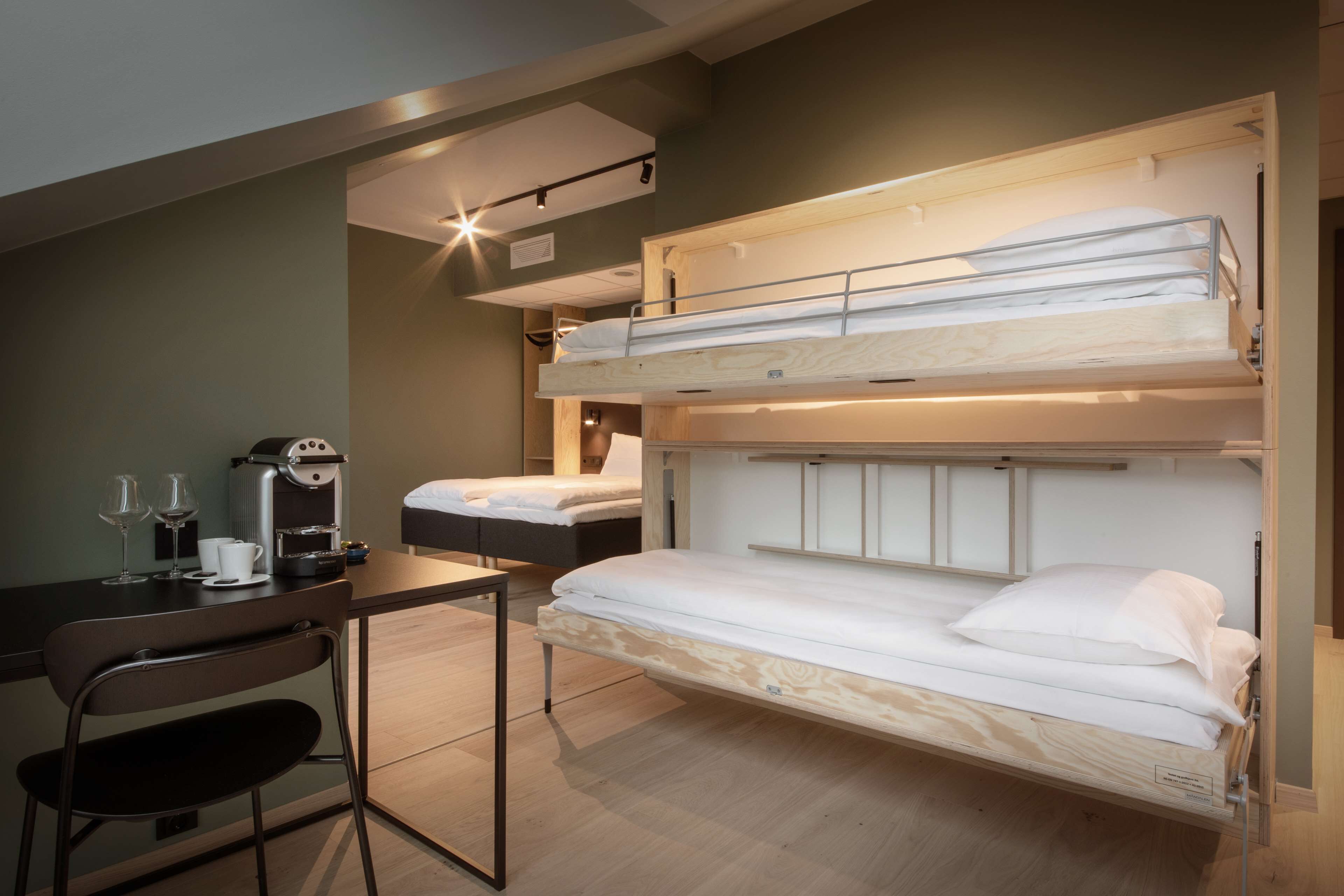 Habitación con literas, un escritorio, una silla, una cafetera y dos copas de vino.