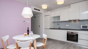 Una cucina moderna con mobili bianchi, forno integrato e microonde. C'è un'area pranzo con un tavolo e sedie bianche, e una lampada a sospensione sopra il tavolo.