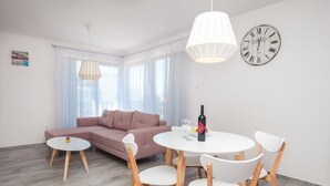 Un soggiorno moderno con un divano, un tavolo da pranzo rotondo con sedie, una sveglia e una lampada a sospensione.