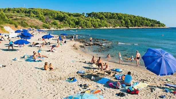 A beach with people sunbathing and swimming, surrounded by blue umbrellas. - Apartments Radojković Lumbarda - Comfort Two Bedroom Apartment with Terrace and Sea View (A2) (Lumbarda)
