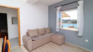 A room with a beige sectional sofa, a window with curtains, a view of a swimming pool, and a wooden floor. - Apartments Radojković Lumbarda - Comfort Two Bedroom Apartment with Terrace and Sea View (A2) (Lumbarda)