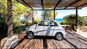 Ein klassischer Wagen steht unter einer Holzpergola mit Blick auf das Meer.