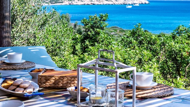 Ein Esstisch, gedeckt für ein Frühstück, mit Blick auf das Meer und die Hügel.