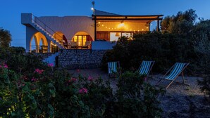 Ein modernes Haus mit Naturstein-Fassade, einer Treppe und einem Balkon mit Lichterketten. Auf der Terrasse befinden sich zwei Lounge-Stühle.
