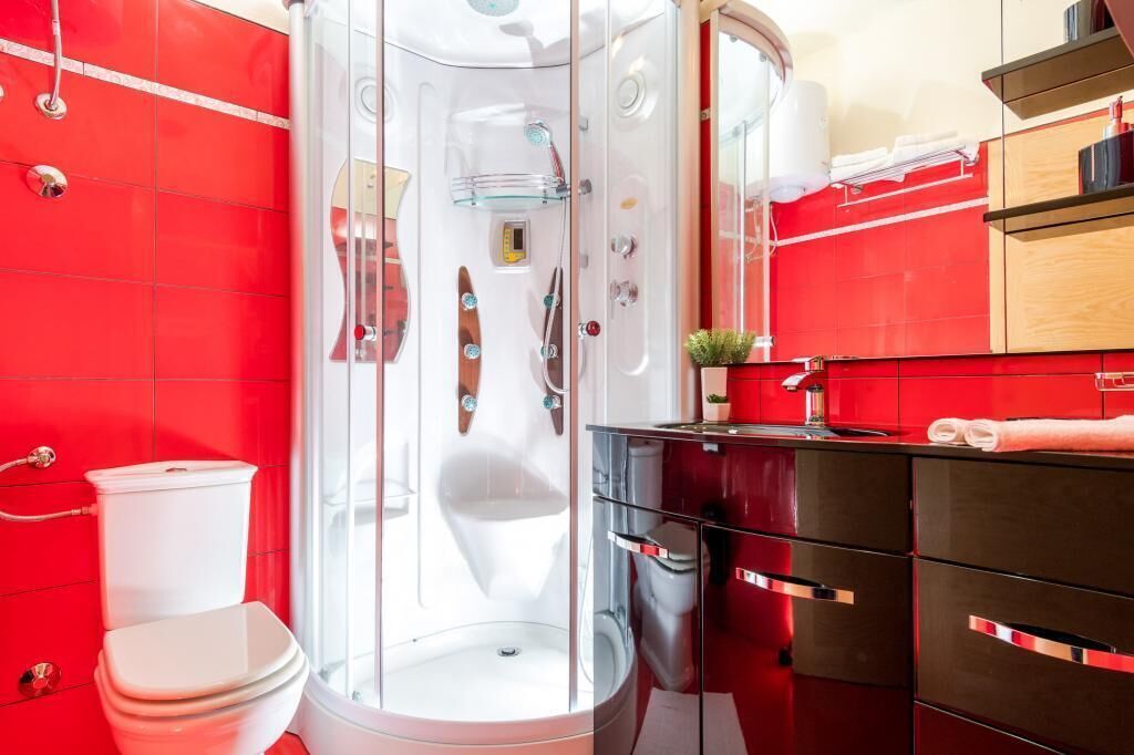 A modern bathroom with a glass-enclosed shower, a white toilet, and a red-tiled wall.