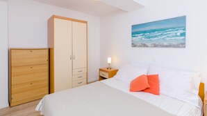 Une chambre à coucher avec un lit, une table de chevet, une armoire et un tableau représentant l’océan accroché au mur.