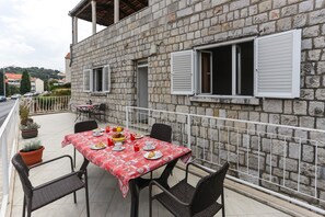 A stone building with a balcony table set for a meal, featuring chairs and potted plants.