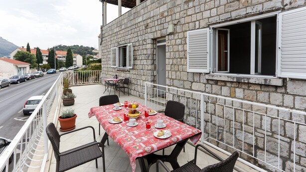 A balcony with a table set for breakfast, overlooking a street with parked cars and buildings in the background.