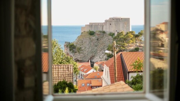 A view of a coastal town with a prominent fortress-like structure on a cliff, surrounded by buildings with red-tiled roofs. - Apartments Cava Dubrovnik - Premium Studio with Patio and Sea View (Dubrovnik)