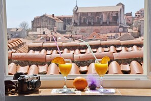 A camera on a windowsill with two glasses of orange juice and an orange.