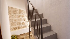Una scala con un muro in pietra su un lato e un muro liscio sull'altro, che conduce a un pianerottolo con pavimento in legno.