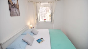 Una camera da letto con un letto, cuscini, una finestra con tende, un comodino, una lampada e un quadro appeso al muro.