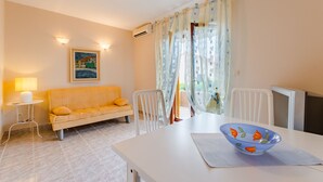 Ein Essbereich mit einem weißen Tisch, einer blauen Schüssel mit orangenen Mustern, einem weißen Stuhl und einem gelben Sofa.
