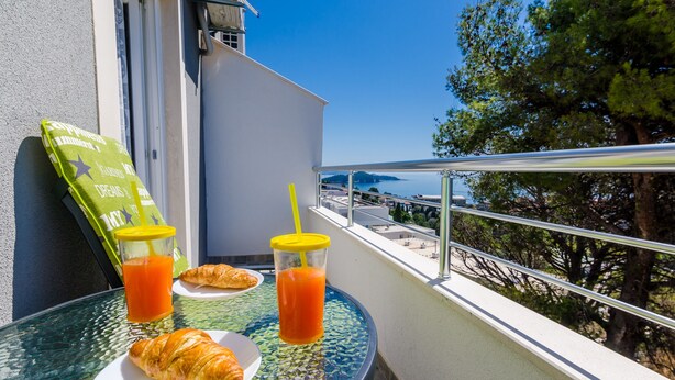 Un balcon avec une table en verre, deux croissants et deux verres de jus d’orange.