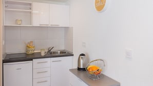 A modern kitchen with white cabinets, a black countertop, and a stainless steel kettle. There is a bowl of fruit on the counter and a sign on the wall that says "JUST SMILE". - Apartments Pomet - Premium Duplex Studio with City View (Puhiera) (Dubrovnik)