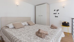 A neatly made bed with a patterned bedspread, a wardrobe, a small table with towels, and a motivational wall quote. - Apartments Pomet - Premium Duplex Studio with City View (Puhiera) (Dubrovnik)