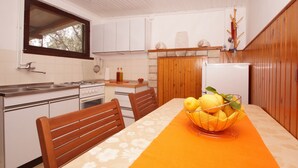 Eine kleine Küche mit weißen Schränken, einem Holztisch mit orangefarbener Tischdecke und einer Obstschale auf dem Tisch.