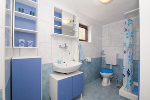 Features a wall-mounted sink, separate toilet, mirror, and shower area with storage.