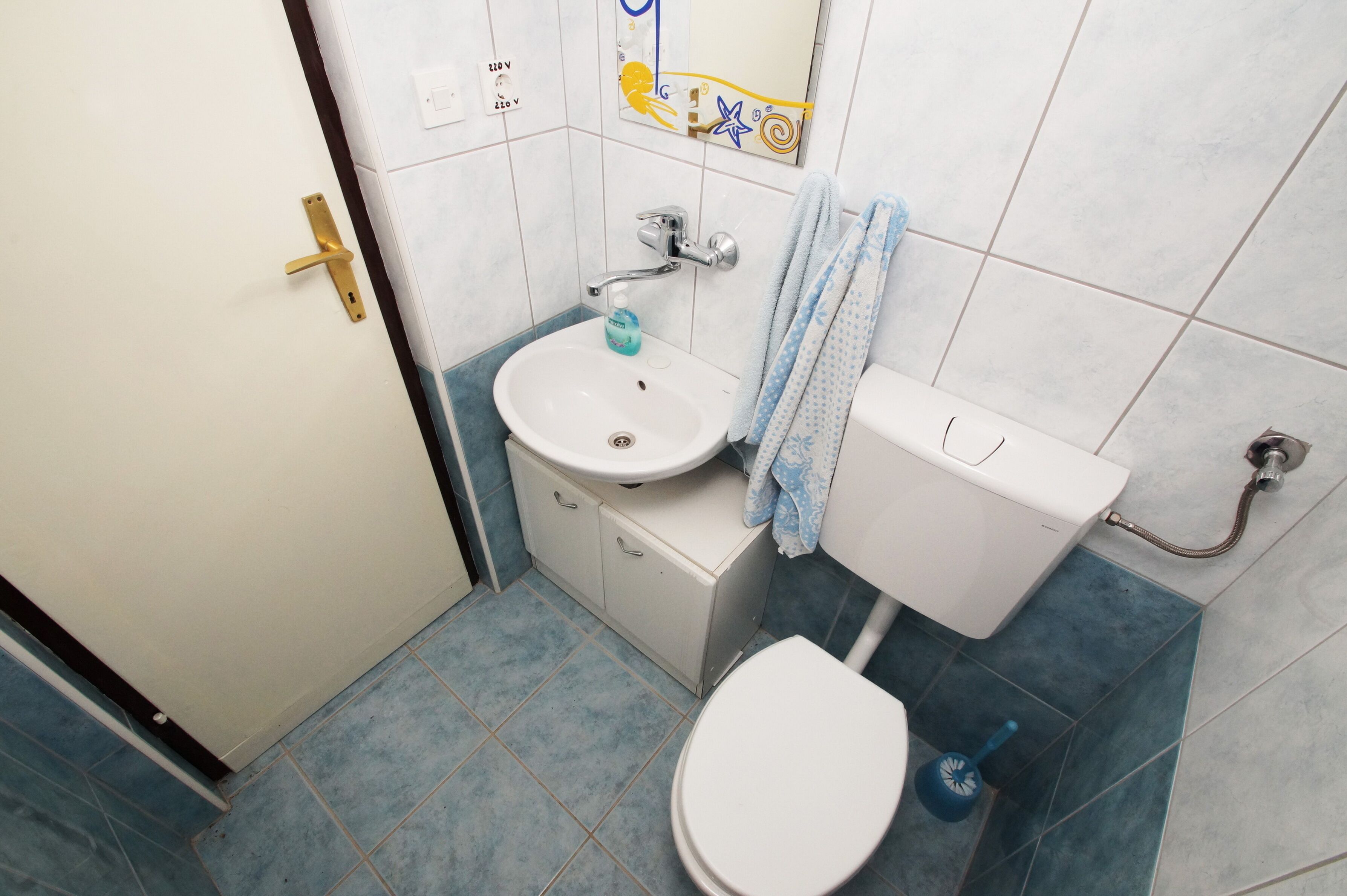 A small bathroom with a white toilet, a sink with a soap dispenser, and a towel hanging on the wall.