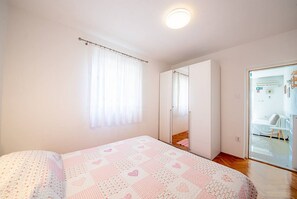A bedroom with a bed, a window with curtains, a wardrobe, and a door leading to another room.