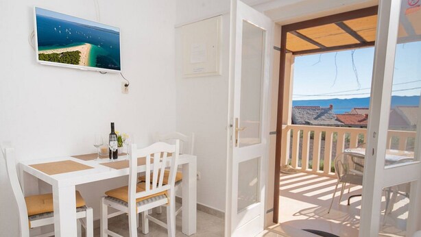 Una habitación con una mesa y sillas blancas, un cuadro de una playa y un balcón con vistas al mar.