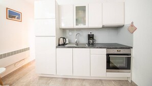 Una cocina compacta con gabinetes blancos, encimera negra, cafetera, hervidor, lavavajillas y horno.