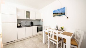 Una cocina compacta con armarios blancos, encimera negra y un comedor con mesa y sillas blancas.