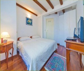 A bedroom with a bed, a desk, a chair, a television, and a door.