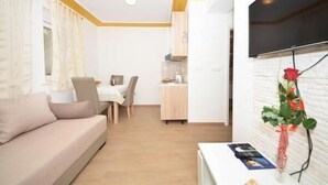 A modern living room with a sofa, a dining area with a table and chairs, a kitchen area, and a mounted TV. - Guest House Mia  - Studio Apartment (Split)