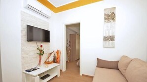 A living room with a beige sofa, a white entertainment unit with a flat-screen TV, and a wall-mounted artwork. - Guest House Mia  - Studio Apartment (Split)