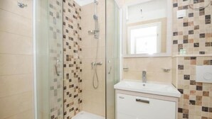 A bathroom with a glass-enclosed shower, a white sink, and a tiled wall. - Guest House Mia  - Studio Apartment (Split)