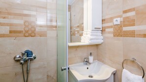 Une salle de bain avec une porte de douche en verre, un lavabo avec un porte-serviettes et un miroir au-dessus du lavabo.