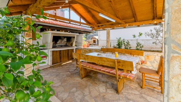 Une terrasse extérieure avec une table et des bancs en bois, un sol en pierre et un mur en pierre.