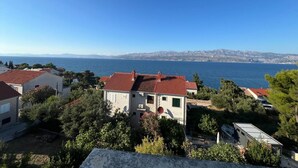 Un quartier résidentiel situé sur la côte, avec des maisons aux toits recouverts de tuiles rouges, entourées de verdure, et offrant une vue sur la mer et les montagnes lointaines.