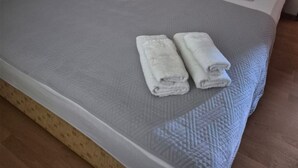 Un lit bien fait, recouvert d’une couverture grise et surmonté de deux serviettes blanches enroulées.