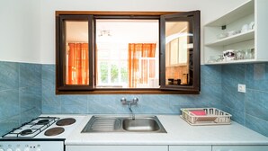 A kitchen with a gas stove, a sink, and a window with curtains. - Apartments Klis -Two-Bedroom Apartment with Terrace (Soline)