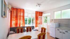 A dining area with a table and chairs, a kitchen with white cabinets, and a view of greenery outside. - Apartments Klis -Two-Bedroom Apartment with Terrace (Soline)