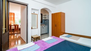 A room with two beds, a wooden wardrobe, a small kitchen area, and a dining area with chairs and a table. - Apartments Klis -Two-Bedroom Apartment with Terrace (Soline)
