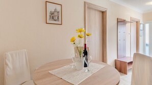 A round table with a vase of yellow flowers, two wine glasses, and a bottle of wine. There are two upholstered chairs around the table. A framed picture hangs on the wall above the table. - Apartments Fidelis - Two Bedroom Apartment with Terrace and Garden View (Okrug Gornji)