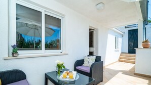 A balcony with wicker furniture, a glass table with breakfast, and a view of the sky.