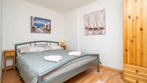 A bedroom with a bed, wooden floor, a nightstand, a lamp, and two paintings on the wall.