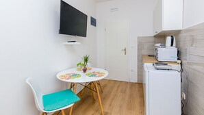 A small kitchenette with a microwave, a refrigerator, and a white cabinet. There is a small table with a potted plant and a chair. - Apartments Saint Mary - Studio Apartment (Apt. 2) (Dubrovnik)