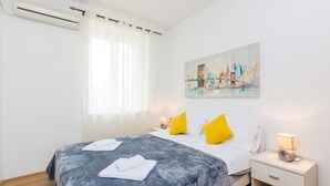 A hotel room with a bed, a nightstand, a lamp, a painting, and an air conditioning unit. - Apartments Saint Mary - Studio Apartment (Apt. 2) (Dubrovnik)