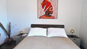 A neatly made bed with white linens, a painting of a woman on the wall, a bedside lamp, and a vase with dried branches. - Villa Katarina - Comfort Double Room with Terrace (Ground Floor) (Dubrovnik)