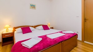 A neatly made bed with white and pink bedding, a wooden nightstand with a lamp, and a wooden door. - Guesthouse Matusic - Double Room (Dubrovnik)