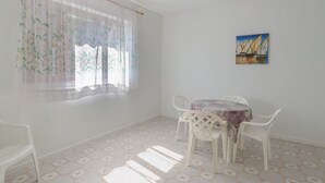 Une pièce comprenant une table à manger, des chaises, une fenêtre avec des rideaux à motifs floraux et un tableau accroché au mur.